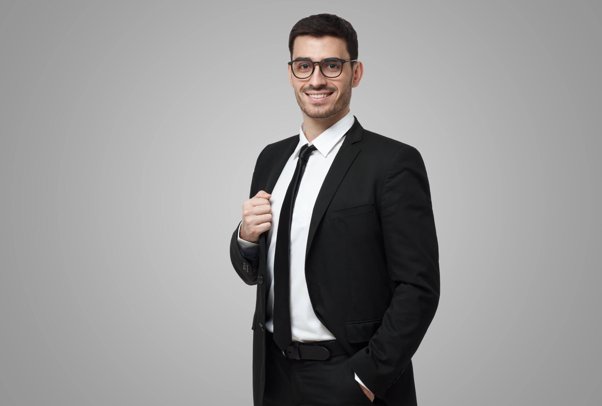 Half-length of smiling confident guy in black suit, white shirt and tie looking at camera